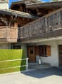 A two-story wooden house with a balcony, garage, and well-maintained garden.