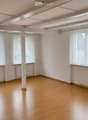 Empty room with wooden flooring, white walls, large windows with sheer curtains, radiators, and exposed ceiling beams.