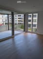 Empty room with wooden flooring and large glass sliding doors leading to a balcony. The balcony has a tiled floor and metal railing.