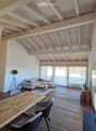 Open-concept living and dining area with exposed wooden beams, white sofa, coffee table, dining table, and chairs.