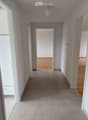 Empty hallway with tiled floor and wooden flooring visible in adjacent rooms, white walls, and a ceiling light fixture.