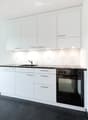Modern kitchen with white cabinets, black countertop, stainless steel sink, and built-in oven and dishwasher.