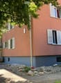 Two-story building with pink facade, white shutters, and a small garden area with rocks and plants.