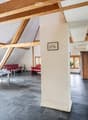 Open-plan living and dining area with exposed wooden beams, modern furniture including a red sofa, dining table with chairs, and a small stool.