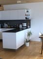 Modern kitchen and dining area with white cabinets, black countertops, a central island, a dining table with chairs, and a pendant light.