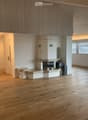 Empty room with wooden flooring, white walls, and a fireplace with a stone surround. The room has large windows and a glass door leading to another space.