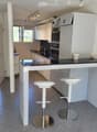 Modern kitchen with white cabinets, stainless steel appliances, black countertops, and two white bar stools at the island.