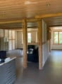 A modern, open-plan office space with wooden beams, a desk, chairs, and a cabinet. The room features a polished tile floor and large windows allowing natural light.