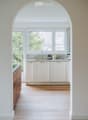 Modern kitchen with white cabinets, wooden flooring, and a large window overlooking greenery. Features a sink, faucet, and small decorative items on the counter.