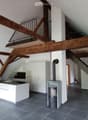 Modern kitchen area with white cabinets, a kitchen island, and a wood stove, featuring exposed wooden beams and a staircase leading to an upper level.