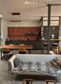 Open-plan living and dining area with a sofa, dining table, chairs, kitchen area, pendant lights, and a plant.