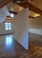 Bright, open attic space with wooden flooring, exposed wooden beams, and a small kitchen area featuring a counter and a stool.