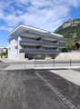 Modern three-story building with balconies, large windows, and a contemporary design, situated in a parking lot with a mountain backdrop.