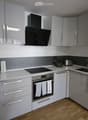 Modern kitchen with grey cabinets, white countertops, and stainless steel appliances including a microwave, coffee maker, toaster, oven, and washing machine. Features a range hood and a sink.