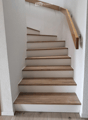 A modern staircase with wooden steps and a matching wooden handrail, set against white walls.