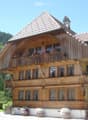 Traditional wooden house with a steep roof, multiple windows, and flower boxes on the balcony and ground level.
