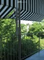 Balcony with metal railing, striped awning, and view of greenery and a distant church tower.