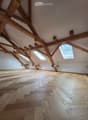 Empty attic space with exposed wooden beams, light-colored wooden flooring, and skylight windows allowing natural light.