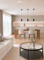 Modern living and dining area with a white sofa, coffee table, dining table with chairs, and a sleek kitchen area in the background.