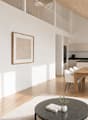 Open-concept living and dining area with light wood flooring, white walls, a modern sofa, coffee table, dining table with chairs, and a sleek kitchen area with cabinets and a sink.