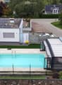 Modern house with a swimming pool in the backyard, surrounded by a fence, with solar panels on the roof and a covered patio area.