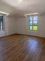 Empty room with wooden flooring, white walls, and large windows offering a view of the outdoors.