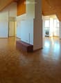 Empty room with wooden flooring, white walls, and a slanted wooden ceiling. A small bench is placed against one wall, and a doorway leads to another room with a visible kitchen area.