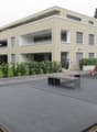 Modern two-story building with beige facade, multiple windows, balconies, and a landscaped courtyard with benches and greenery.
