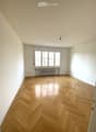 Empty room with wooden floor, white walls, windows with radiators, no furniture