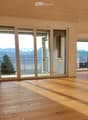 Empty room with wooden flooring and large sliding glass doors leading to a balcony with a scenic view.
