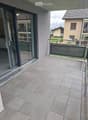 Modern balcony with large grey tiles, glass sliding door, metal railing, and view of neighboring houses.