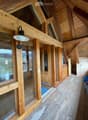 Wooden hallway with large windows, exposed wooden beams, and a modern wall-mounted light fixture.