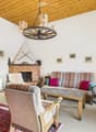 Cozy living room with a fireplace, patterned sofa, wooden coffee table, armchair, television, and decorative picture frames on the walls.