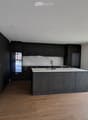 Modern kitchen with dark cabinets, a central island, and large windows overlooking a street with parked cars.
