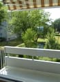 Balcony with white railing, overlooking a green park area with trees and a building in the background.