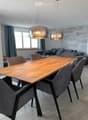 Modern dining area with a wooden table, six grey chairs, a grey sofa, and two pendant lights hanging from the ceiling.
