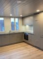 Modern kitchen with light grey cabinets, wooden flooring, and large windows offering a view of the roof.