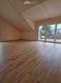 Empty attic room with wooden flooring, large windows, and sliding doors leading to a terrace.