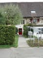 2 story house, brown roof, red door, white walls, hedges, walkway, mailbox