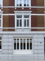 Classic European building facade with red brick upper levels and white plaster lower level, featuring multiple windows with decorative white surrounds and a central wooden door.