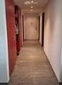 Clean hallway with tiled floor, beige walls, and a closed door at the end. A red wardrobe with hanging clothes is visible on the left side.