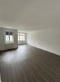 Empty room with wooden flooring, white walls, and large windows with radiators below them.