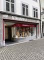 Facade of a shop named "Stampfli Optik" with a glass display window showing various optical items, located on a cobblestone street.