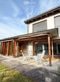 A modern house with a spacious outdoor patio area featuring white chairs and a table, surrounded by a well-maintained lawn and paved pathways.