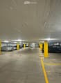 Underground parking area with several parked cars, yellow pillars, and marked parking spaces.