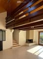 Open-plan living space with wooden ceiling beams, large sliding glass doors leading to a balcony, staircase, and fireplace.