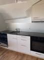 Modern kitchen with white cabinets, black countertops, stainless steel appliances, and wooden flooring.