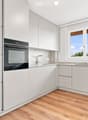 Modern kitchen with white cabinets, wooden flooring, and a large window overlooking a cityscape.