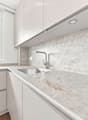 Modern kitchen with white cabinets, marble countertop, and a stainless steel sink with a modern faucet. The backsplash features a textured, light-colored tile design.