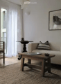 Modern living room with white walls, wooden floor, large windows, balcony access, sofa, coffee table, chair, small table, and picture frame.
